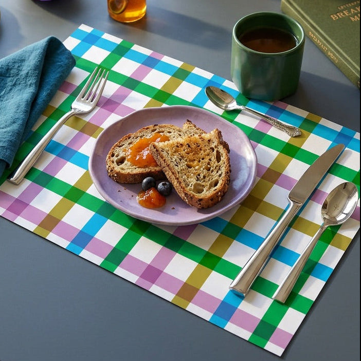 Table setting with a colorful checkered paper placemat, plates with food, and utensils.