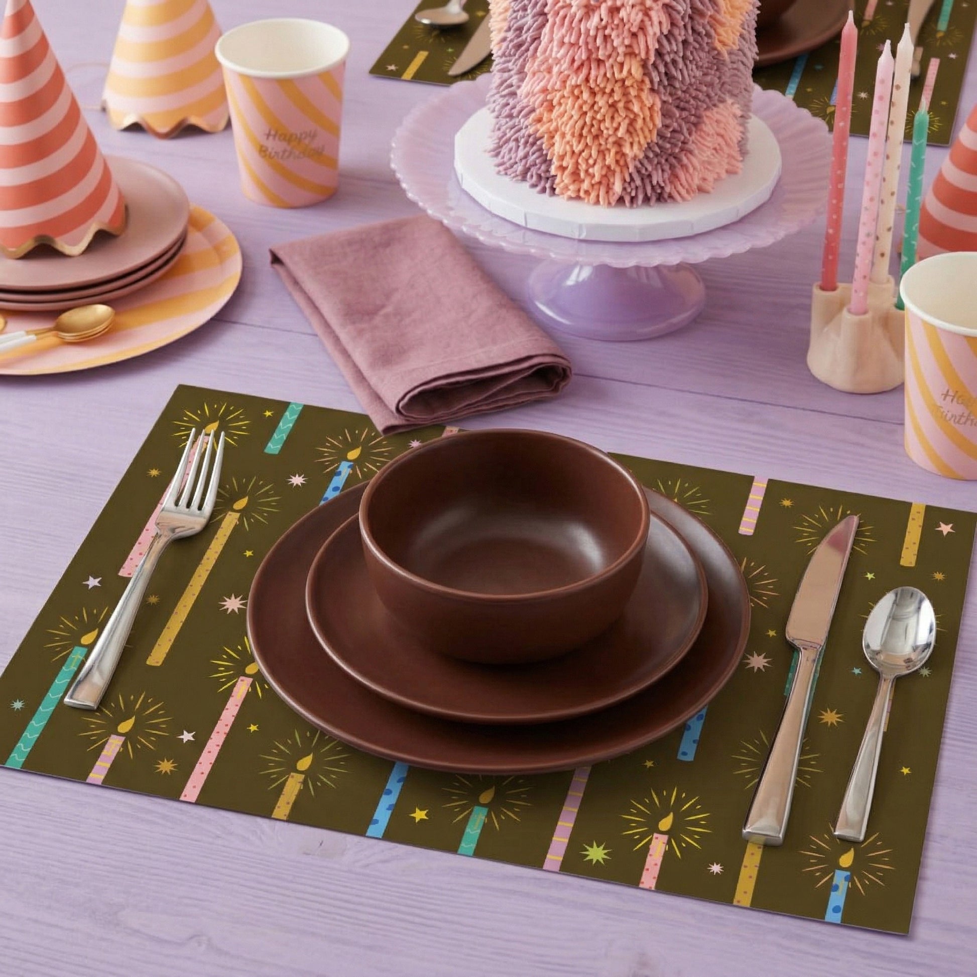 Dinnerware set on a paper placemat with a cake and party cups in the background