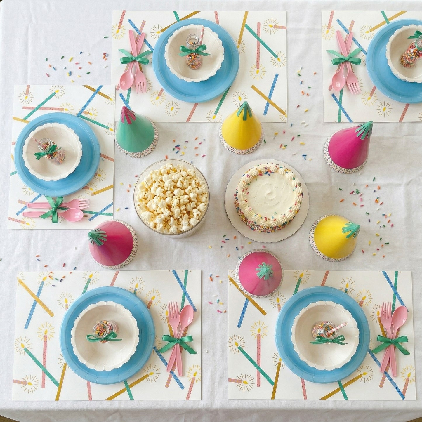 Children's birthday party table with colorful plates, cups, and cake on a paper placemats.
