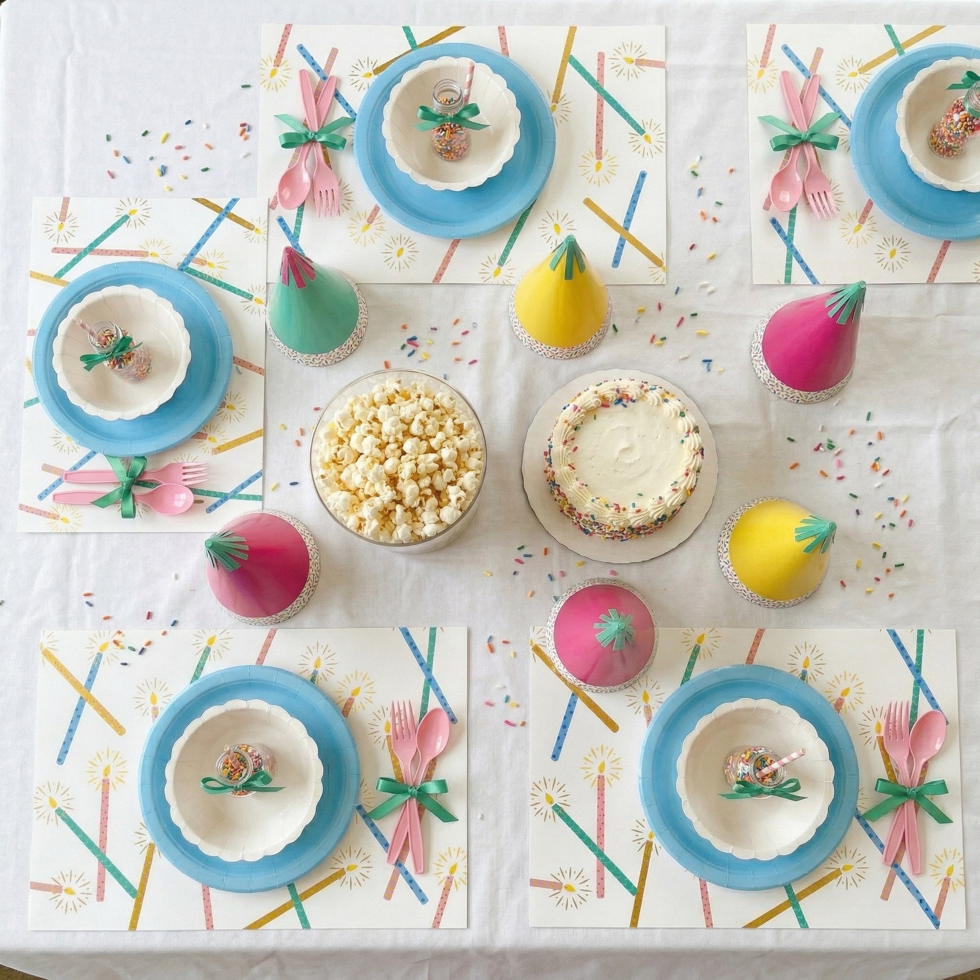 Children's birthday party table with colorful plates, cups, and cake on a paper placemats.