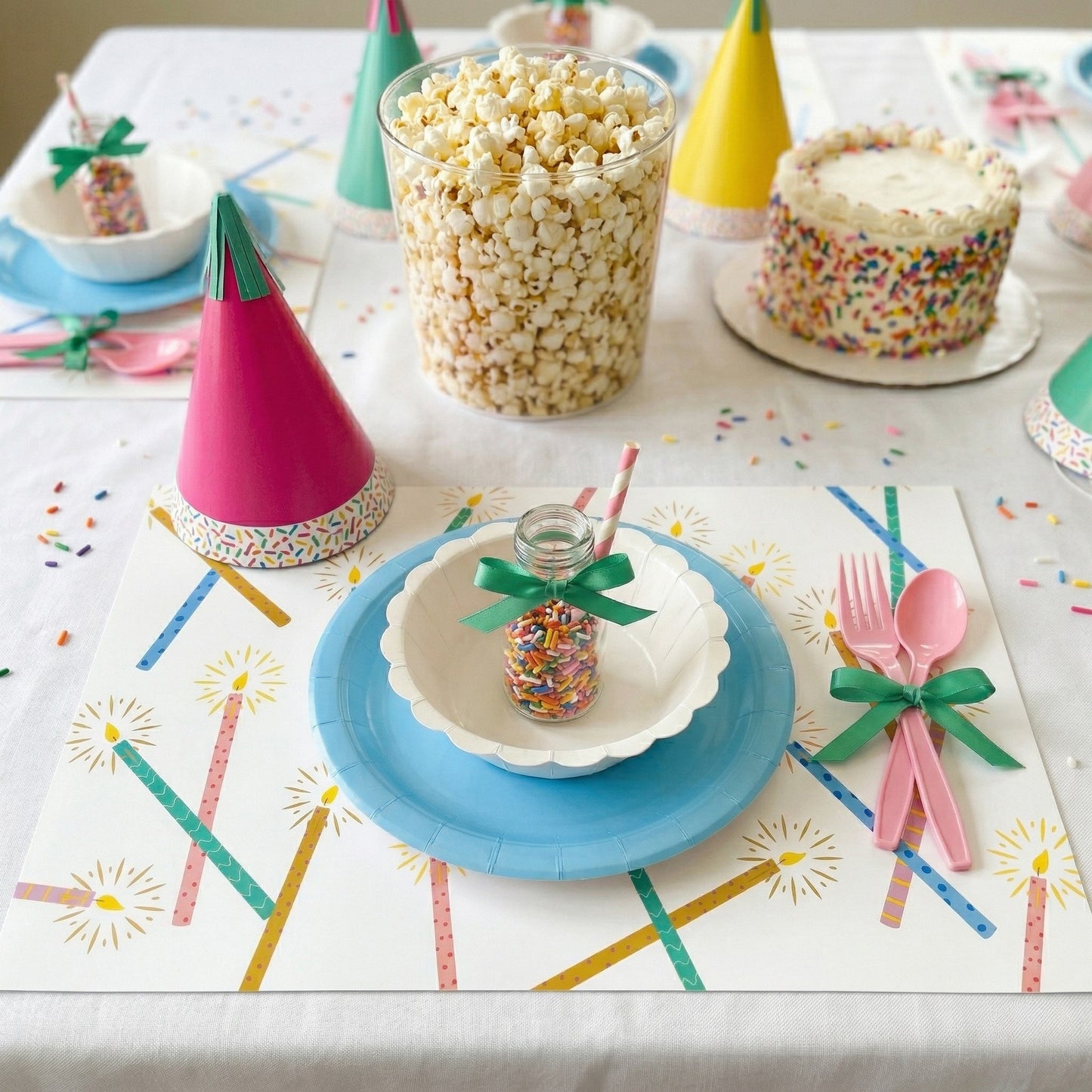 Children's party table setting with colorful plates, cups, and celebration paper placemats.