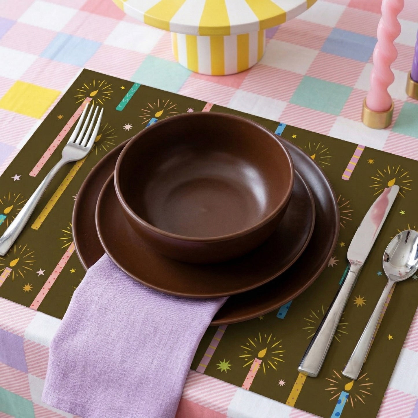 Set of brown ceramic bowls on a colorful paper placemat with cutlery and a checkered tablecloth.