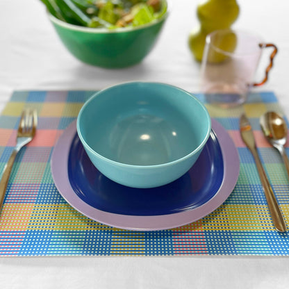Set table with blue bowl, plates, and cutlery on a checkered paper placemat.