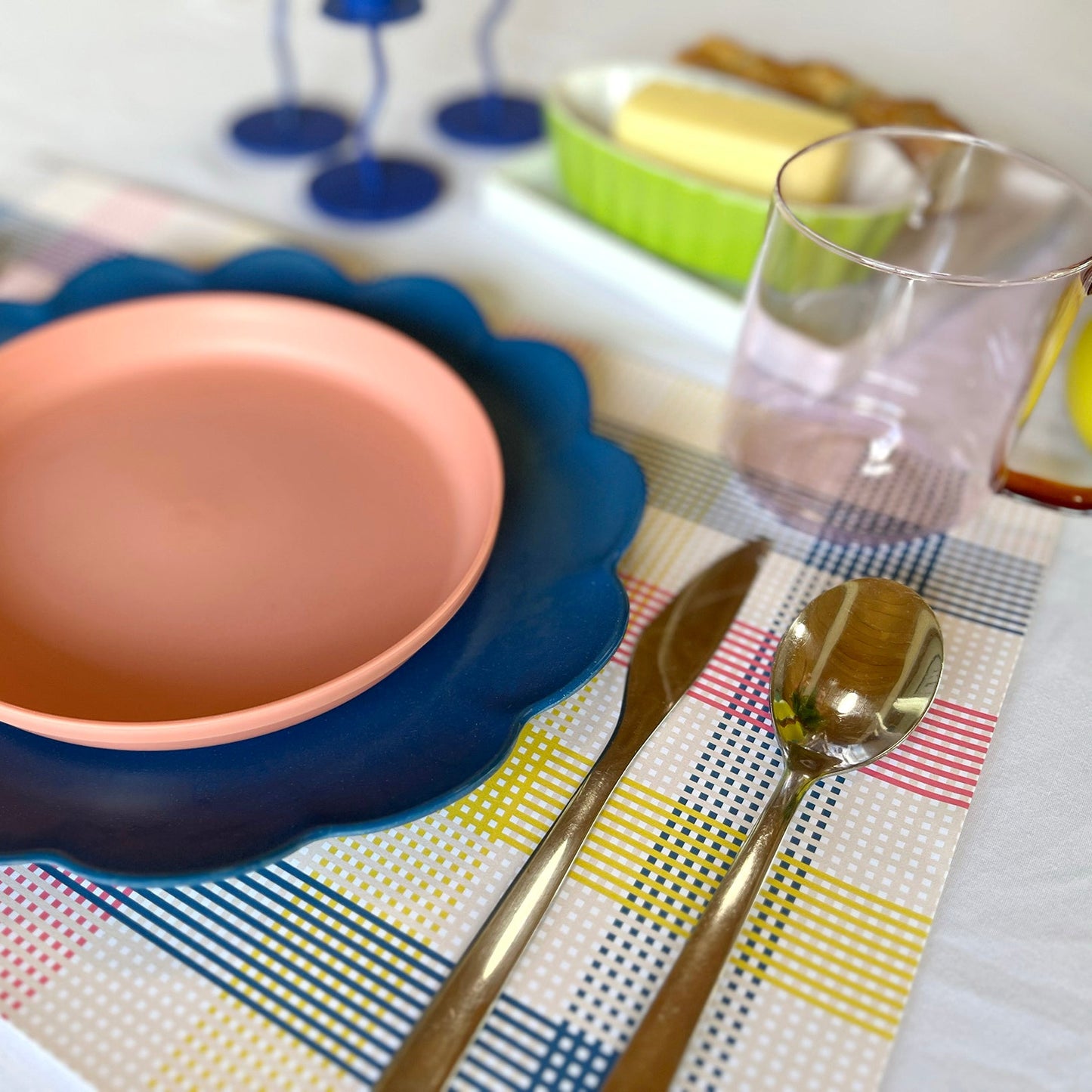Ceramic plate with blue rim on a colorful paper placemat with cutlery and glasses.