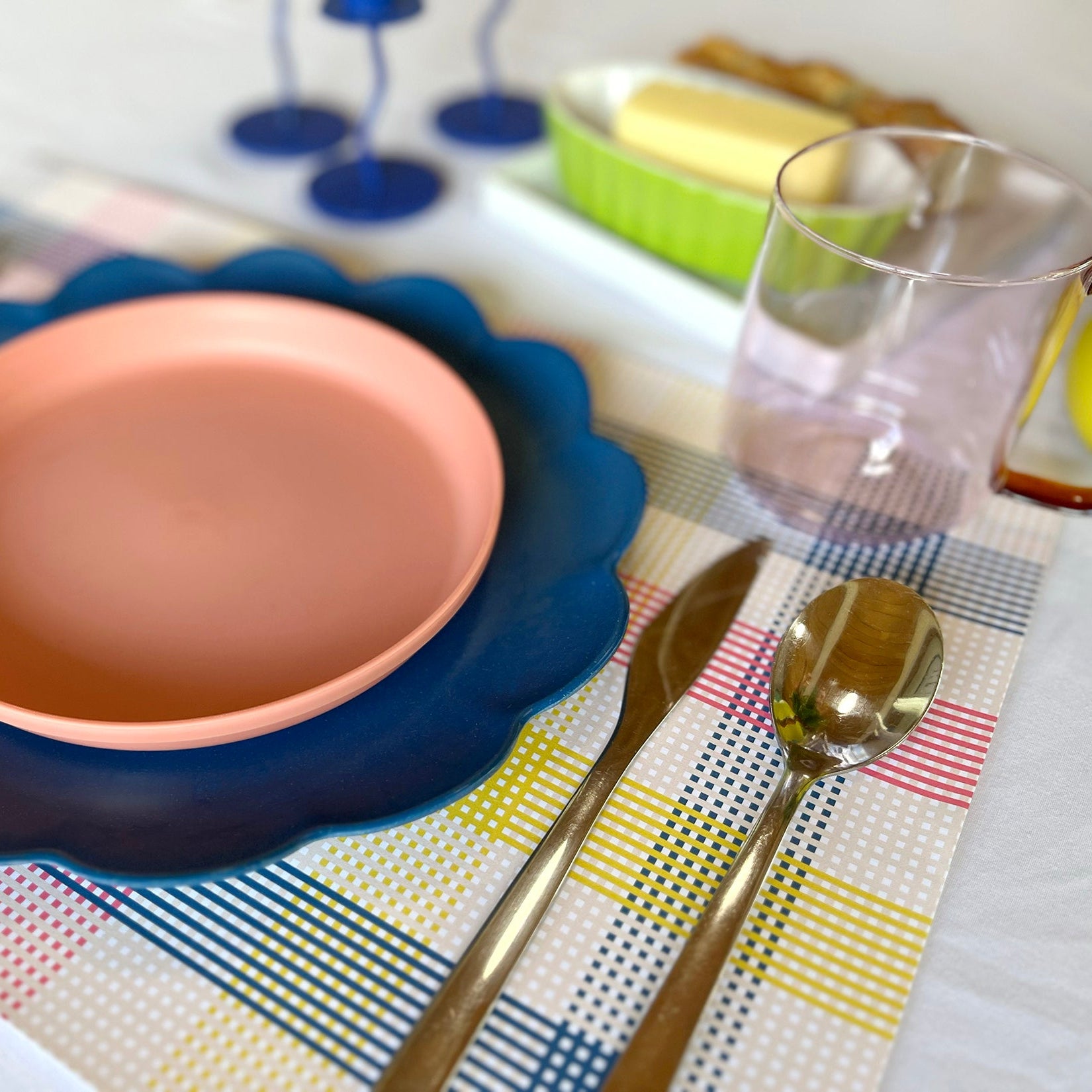 Ceramic plate with blue rim on a colorful paper placemat with cutlery and glasses.