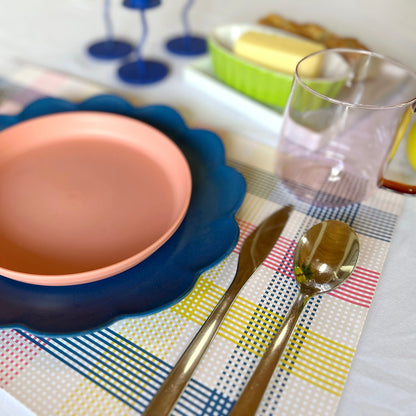 Ceramic plate with blue rim on a colorful paper placemat with cutlery and glasses.