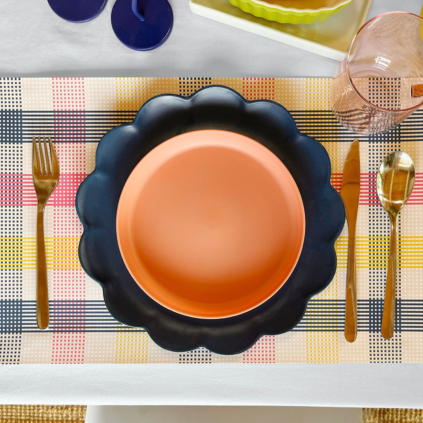 Dinner setting with a black bowl, gold fork, knife, and spoon on a checkered paper placemat.