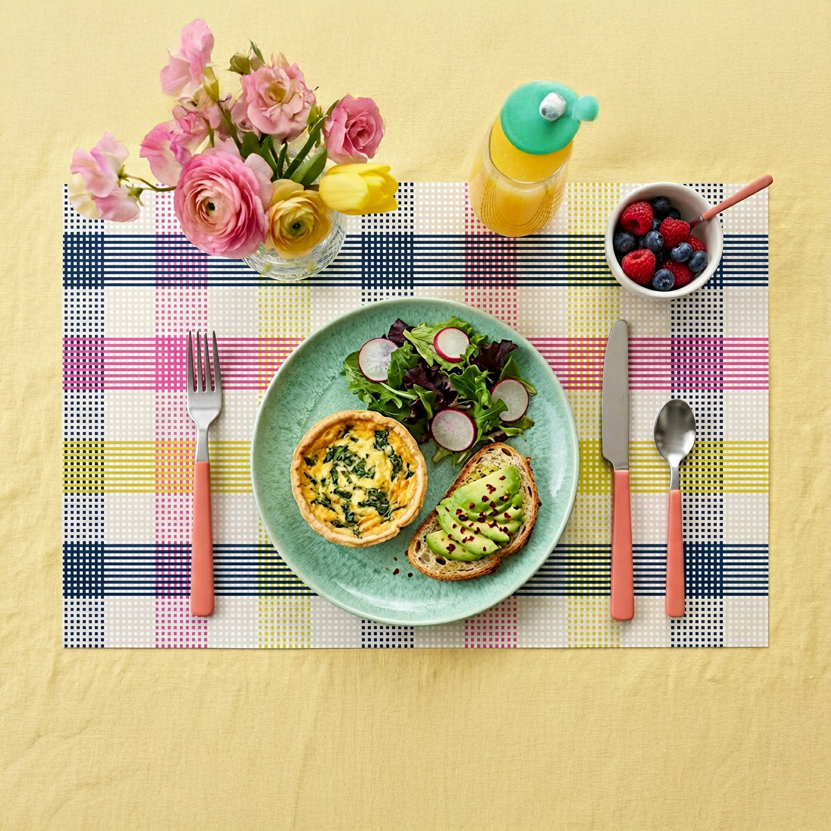 Breakfast setting with a plate of food, flowers, and drinks on a colorful paper placemat.