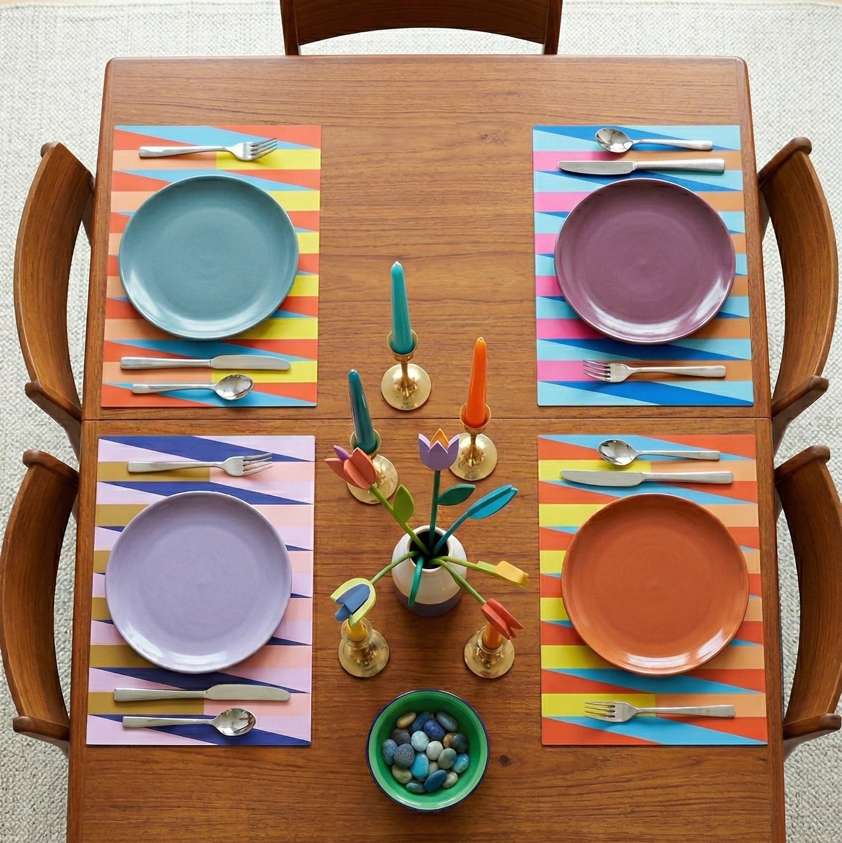 Wooden dining table set with colorful plates and paper placemats, and utensils on a striped tablecloth.