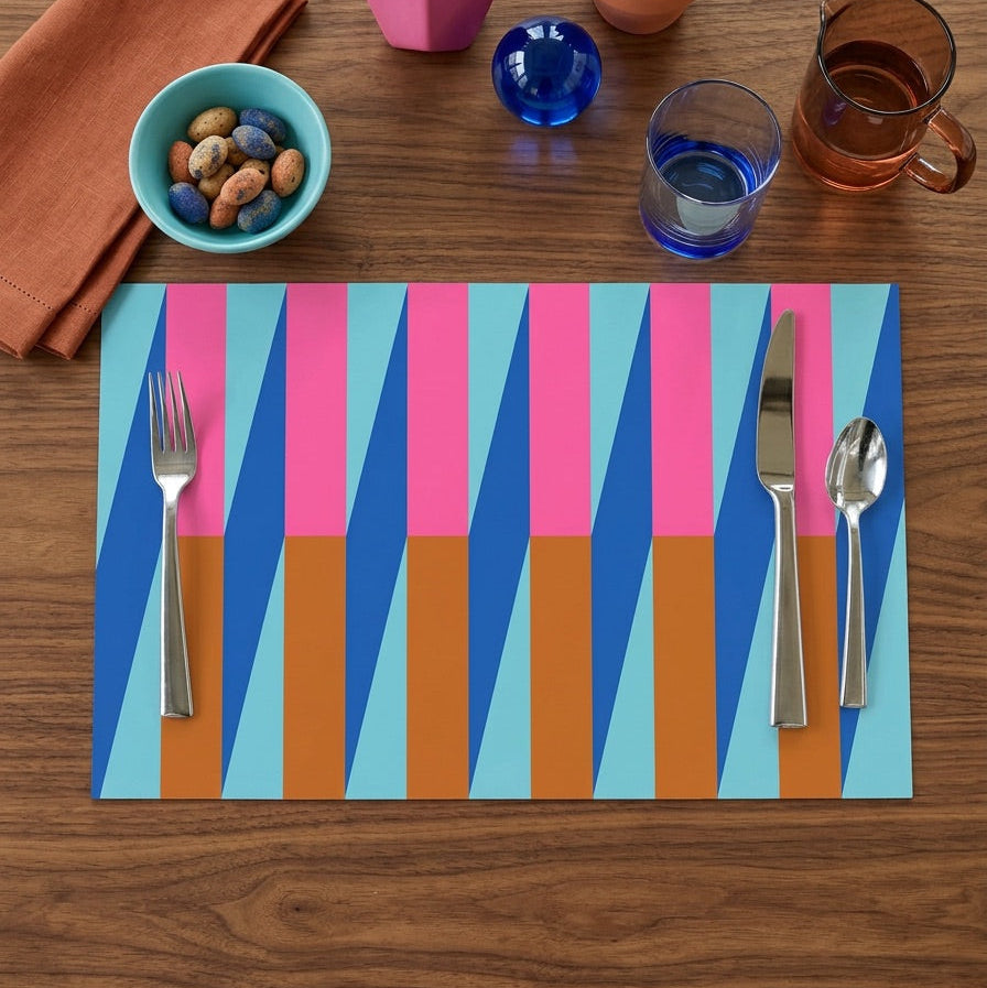Colorful geometric paper placemat on a wooden table with cutlery and small plants.