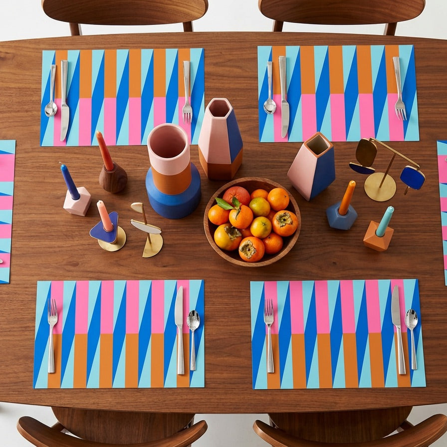 Dining table set with colorful paper placemats, cutlery, and a bowl of fruit.