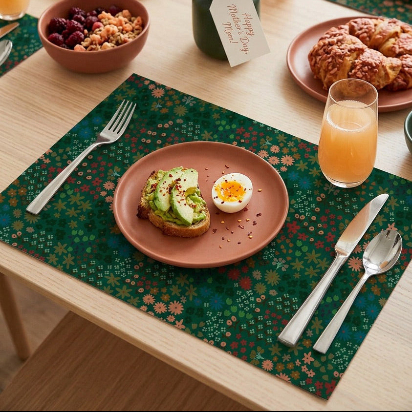 Breakfast table setting with plates of food, glasses of juice, and a vase of flowers with floral paper placemats.