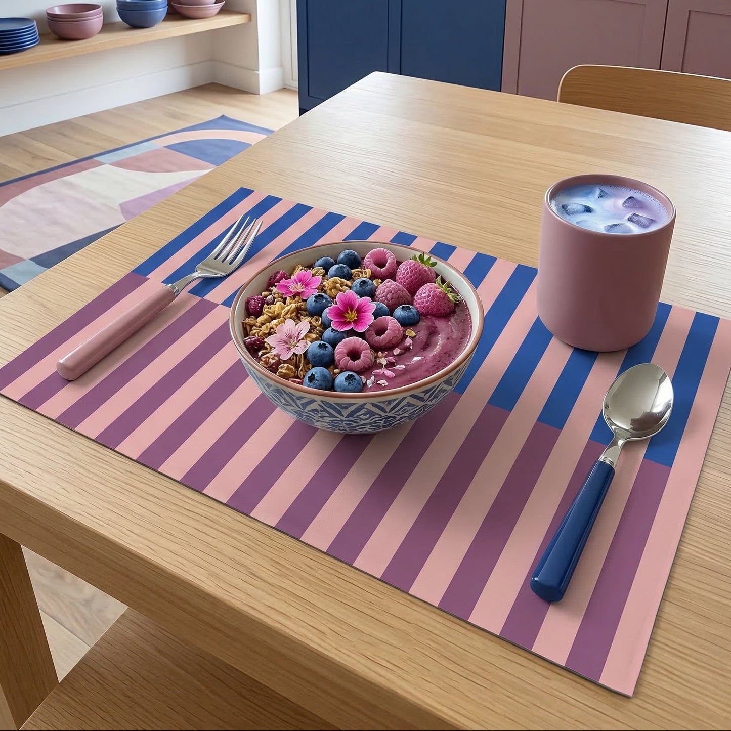Dining table with a bowl of fruit, a cup, and utensils on a striped paper placemat in a kitchen.