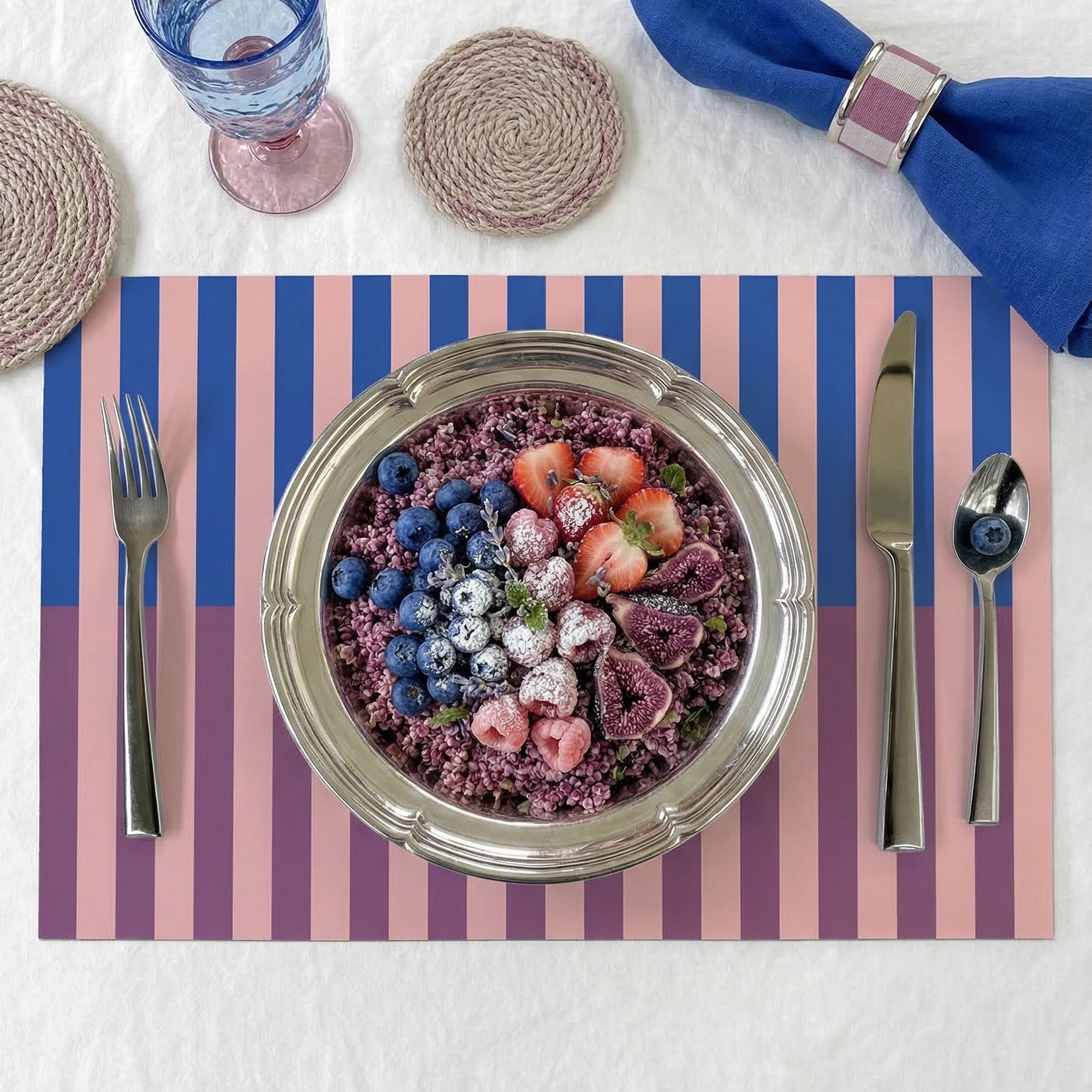 Dinner setting with a bowl of salad on a striped paper placemat, cutlery, and glasses.