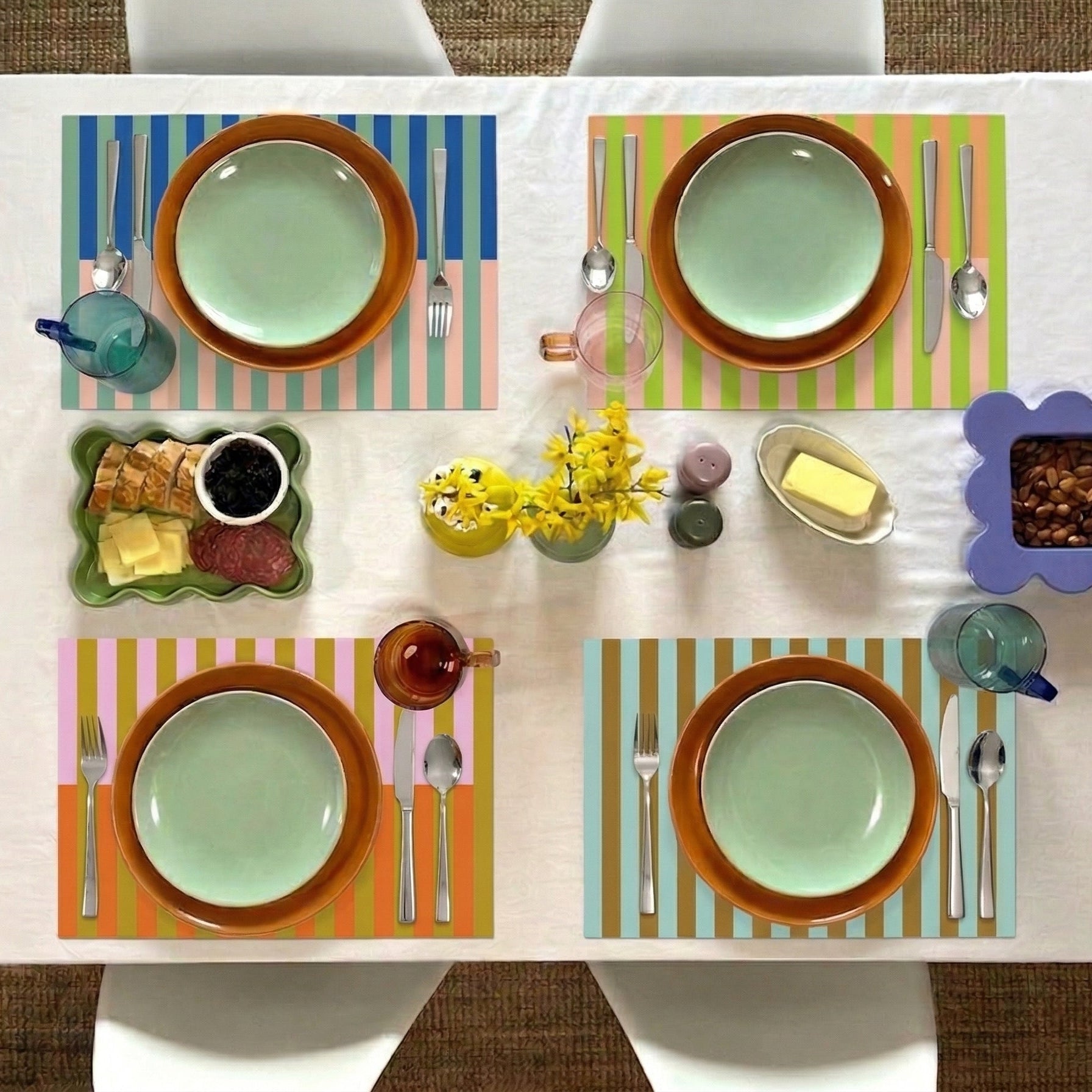 Colorful table setting with plates, cutlery, and small dishes on a striped paper placemat.