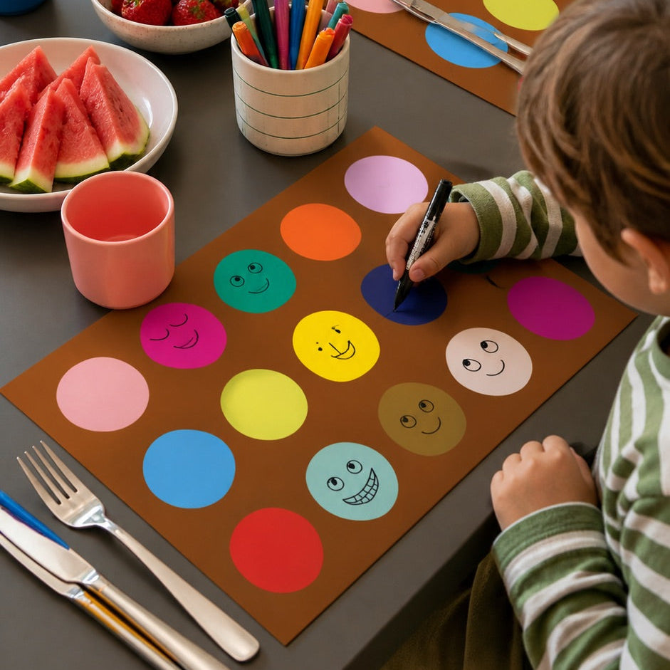 Child coloring on a placemat with a table full of snacks and drinks in a home setting.