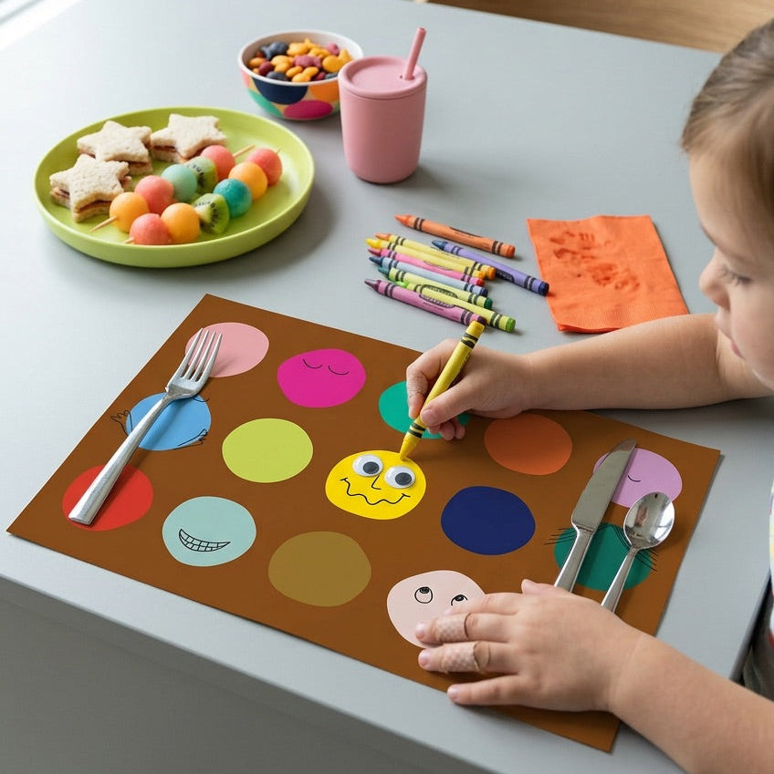 Child coloring on a placemat at a dining table with snacks and utensils.
