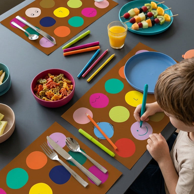 Children's table setting with colorful placemats, cutlery, and snacks in a home setting.