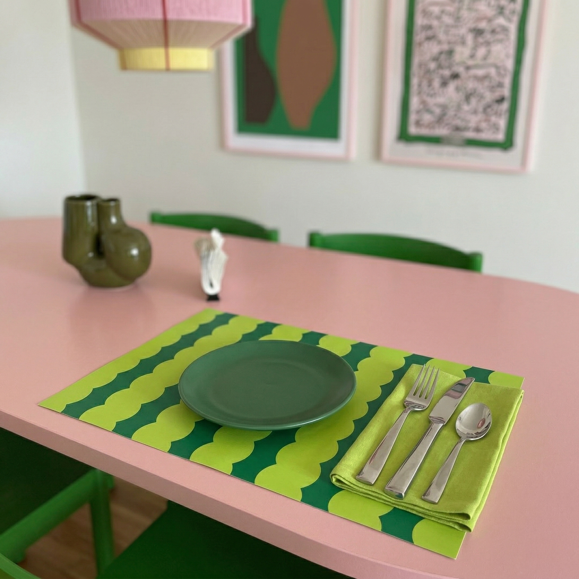 Dining table setting with green plate, cutlery, and paper placemat on a pink table.