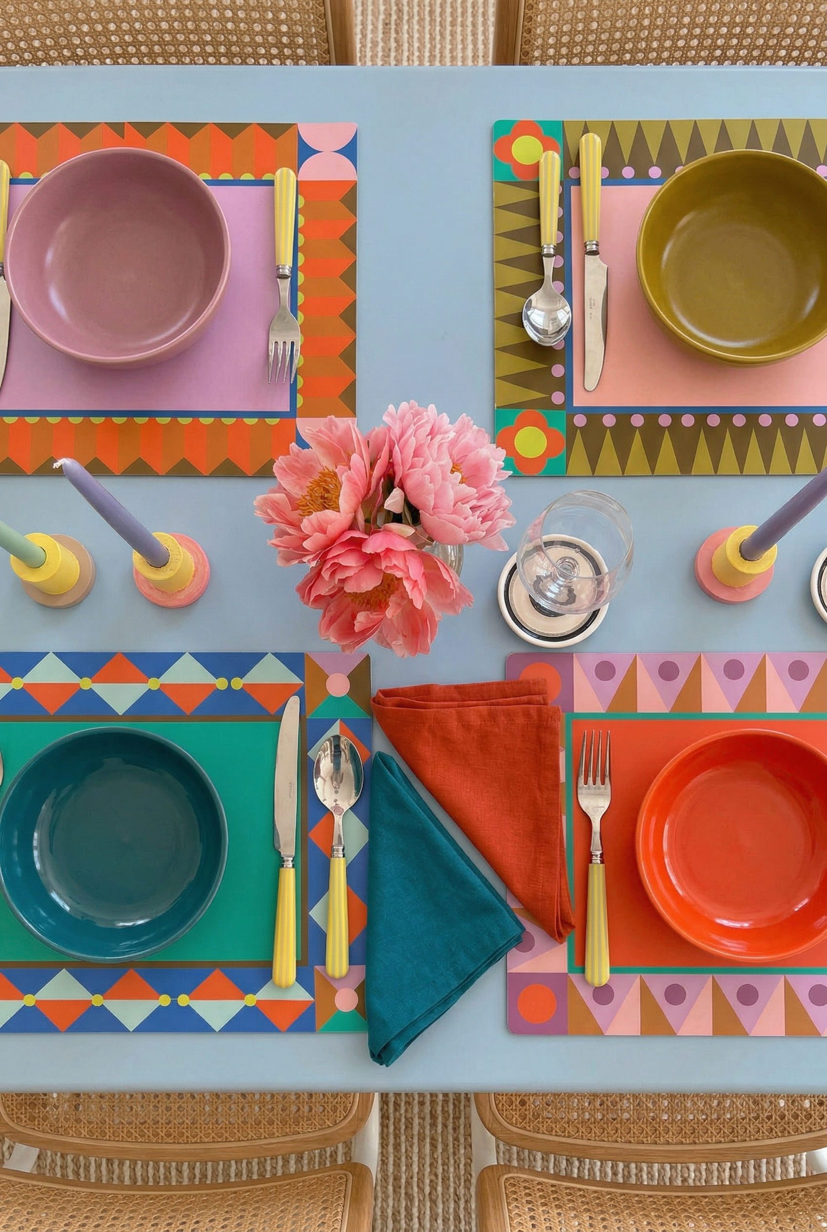 Colorful table setting with geometric paper placemats, plates, and cutlery on a blue table.