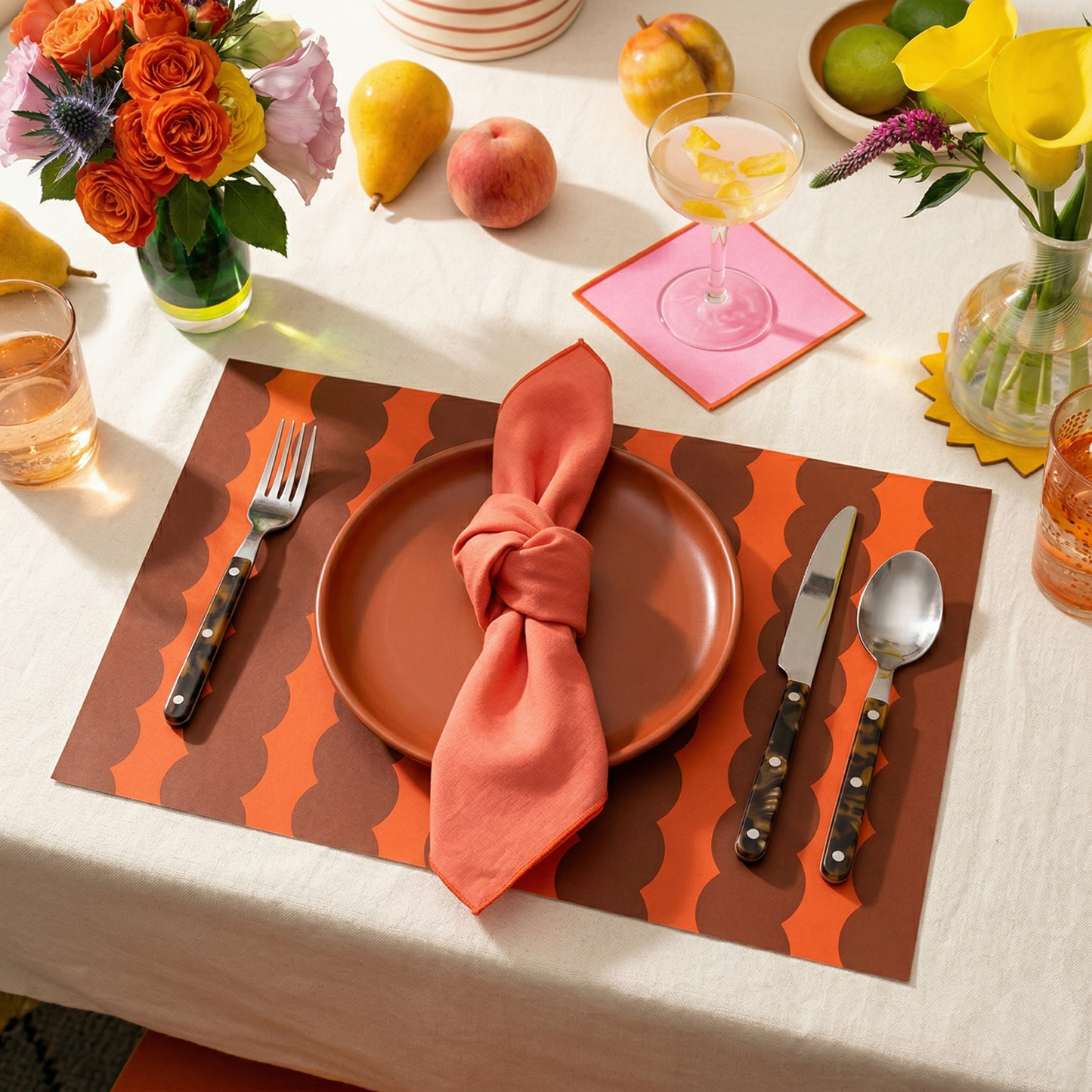 Dining table setting with orange plate, pink napkin, and colorful red striped paper placemats.