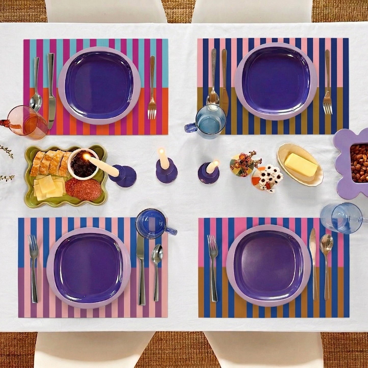 Colorful table setting with purple plates, striped paper placemats, and various tableware on a white table.