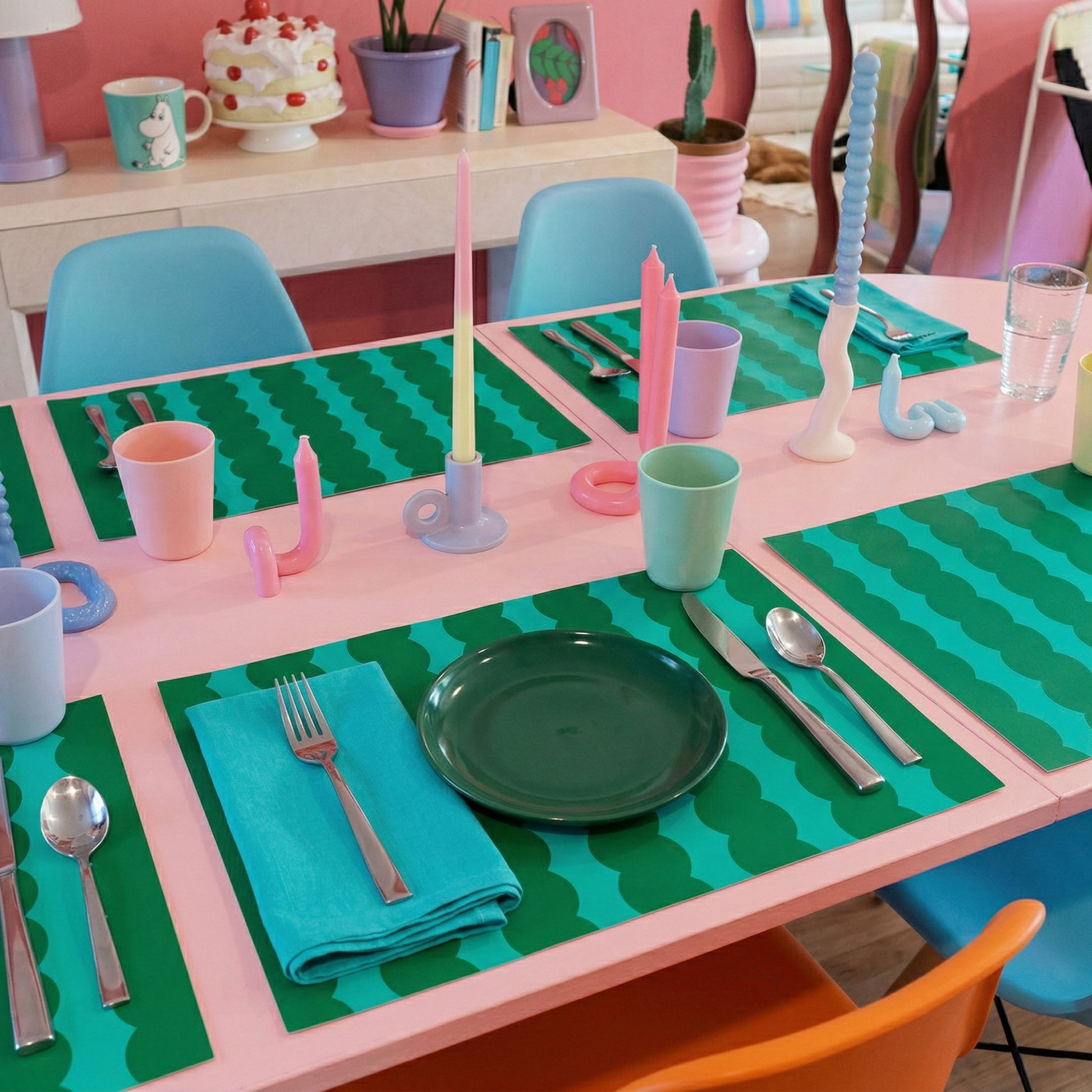Colorful children's table setting with pink and green wavy striped paper placemats, plates, and cutlery.