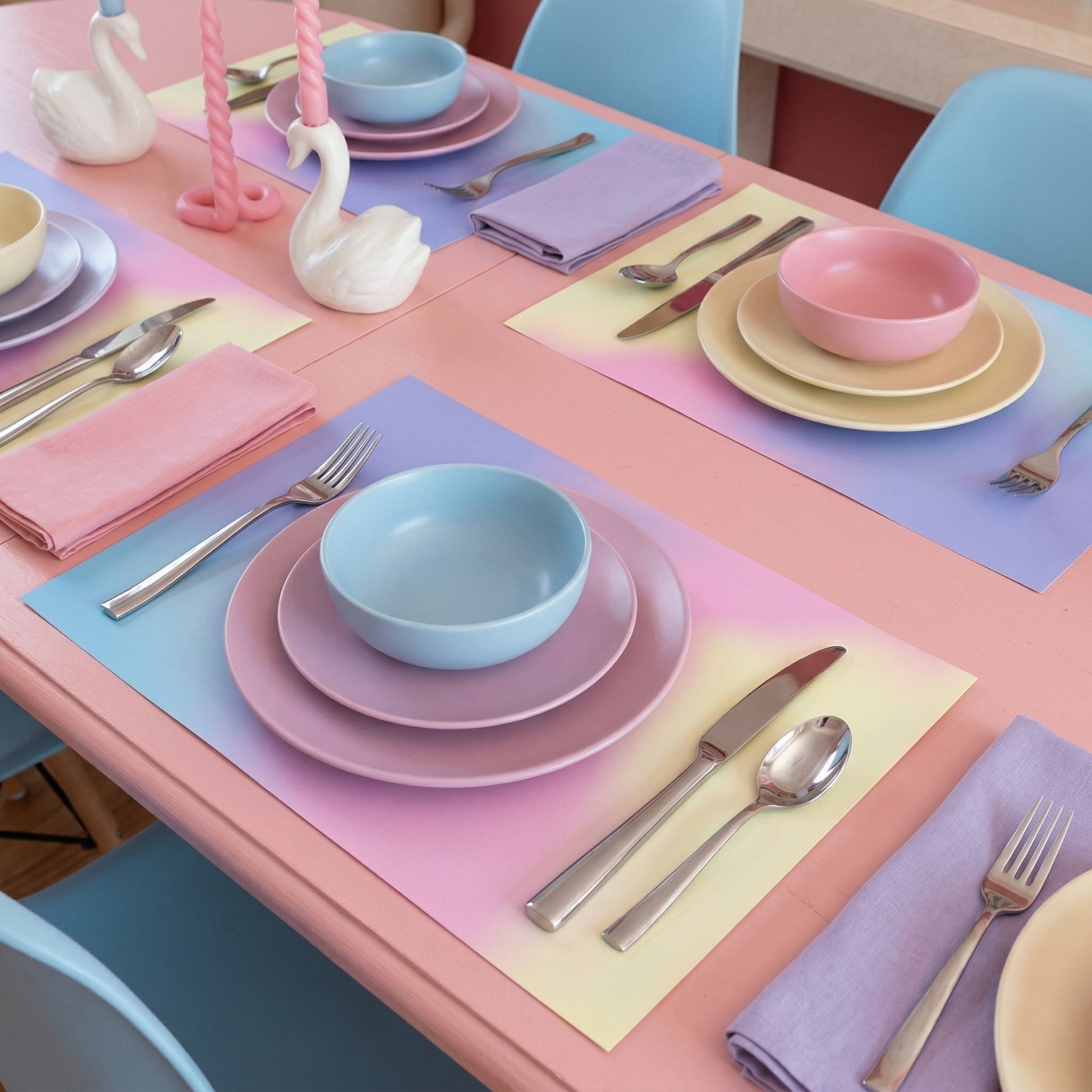 Pastel-colored table setting with plates, bowls, and cutlery on gradient paper placemat.