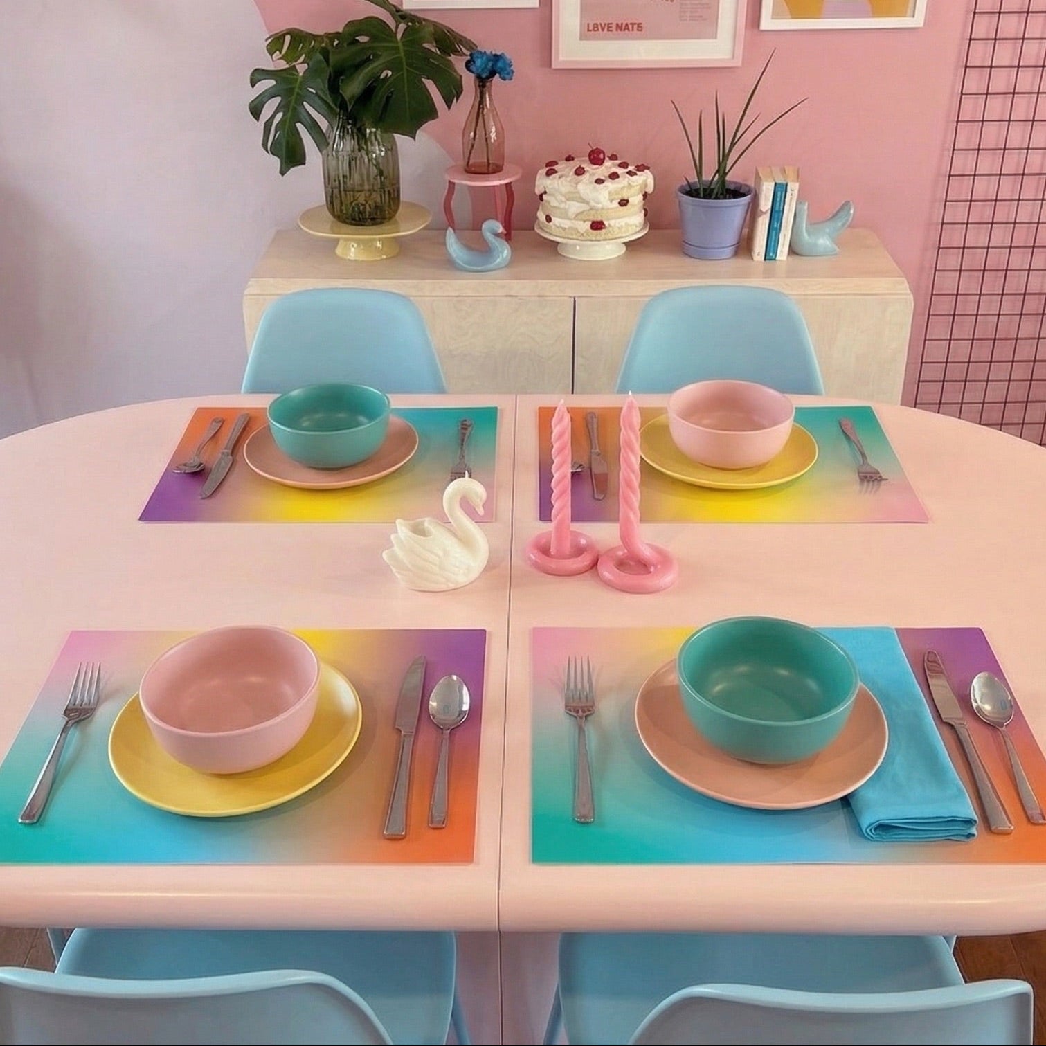 Dining table set with colorful plates, bowls, and utensils on a pink table with colorful paper placemats.