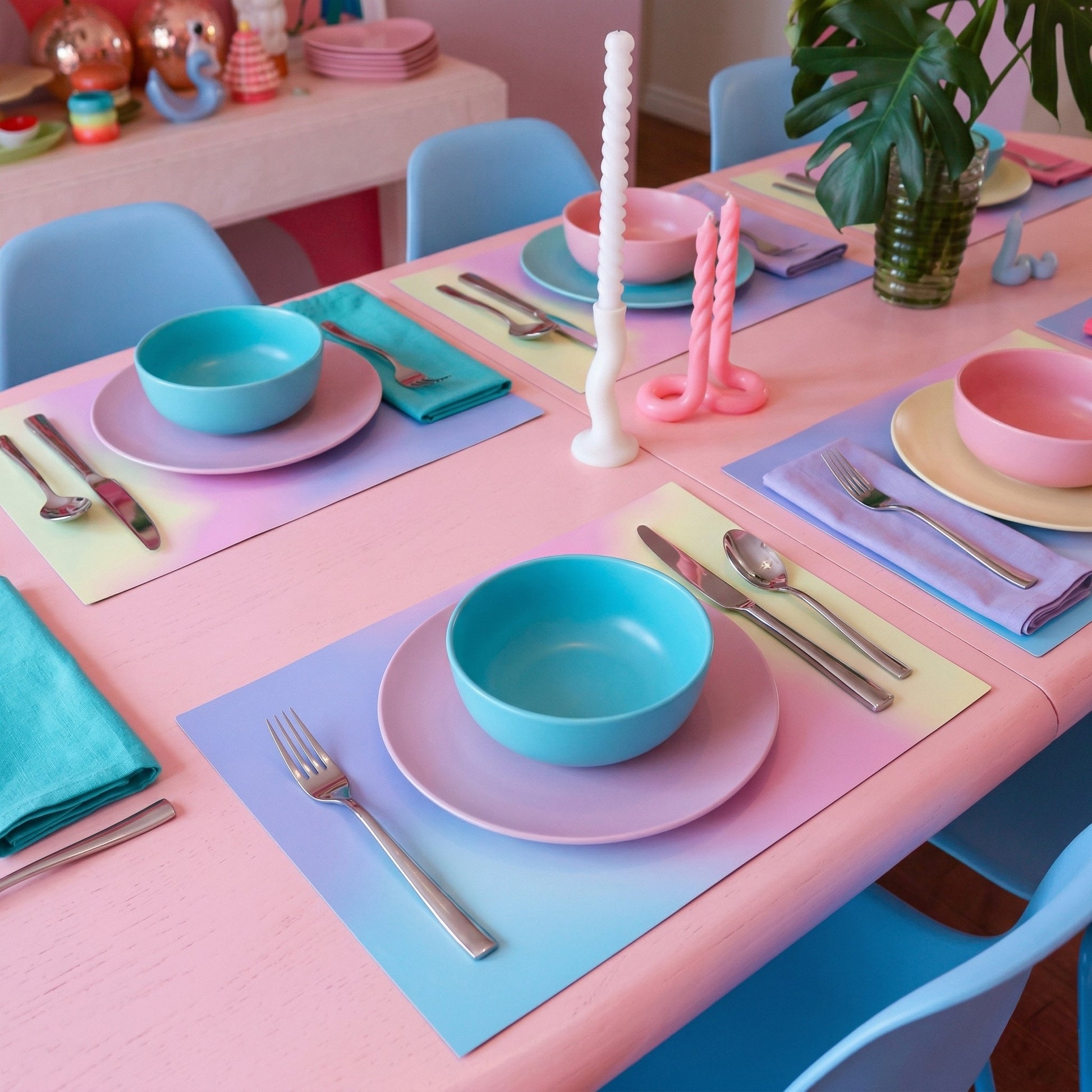 Colorful table setting with pastel-colored plates, bowls, and paper placemats on a pink table.