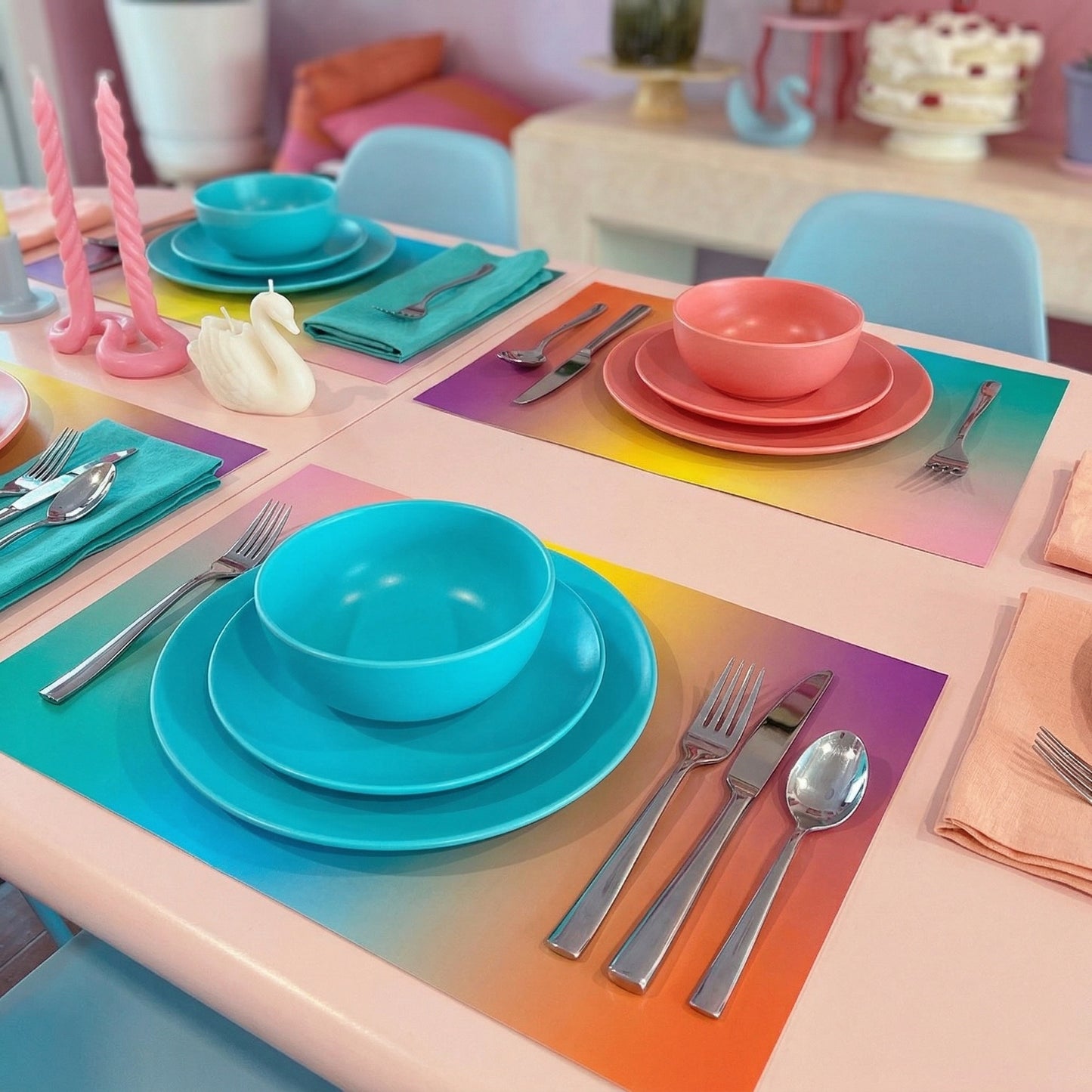 Colorful table setting with turquoise, pink, and orange plates and utensils on a gradient paper placemat.