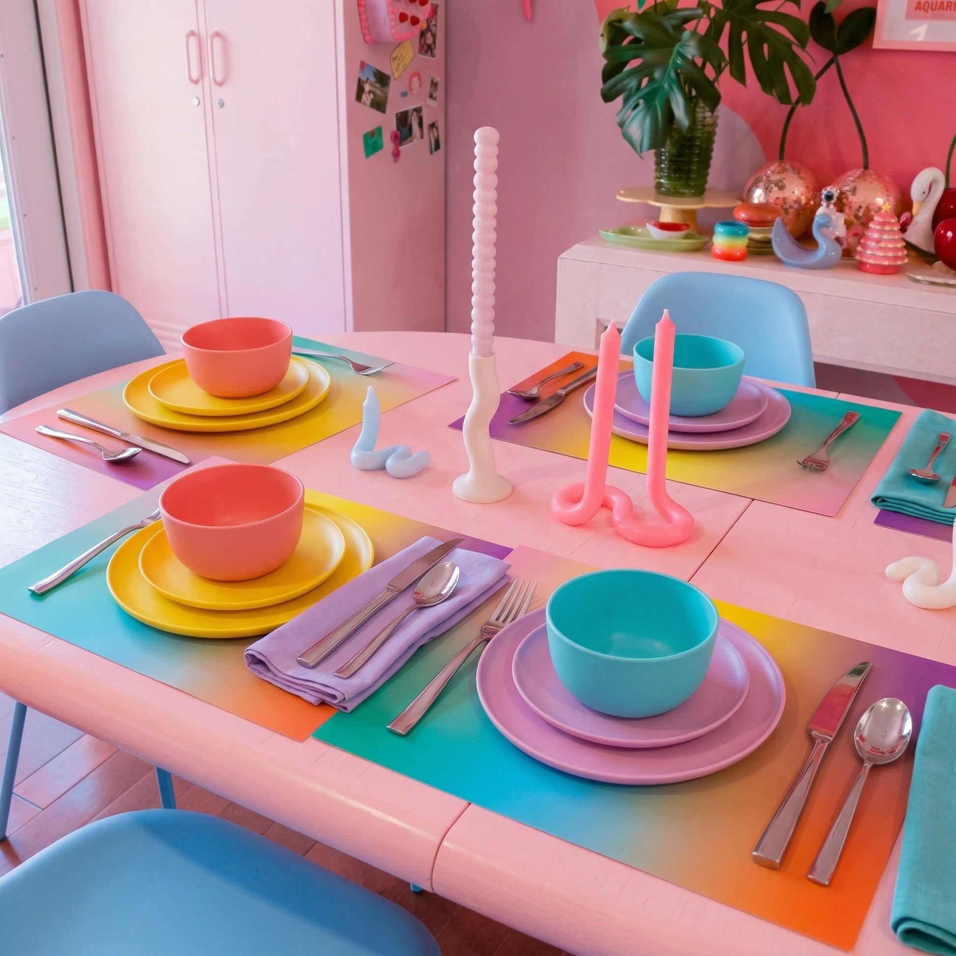Colorful table setting with pastel plates, bowls, and utensils on colorful paper placemats.