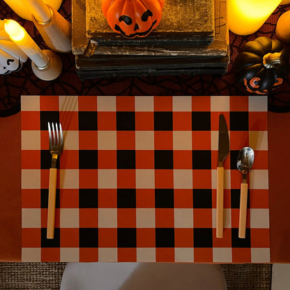 Halloween-themed table setting with checkered placemat, utensils, and decorative pumpkins.