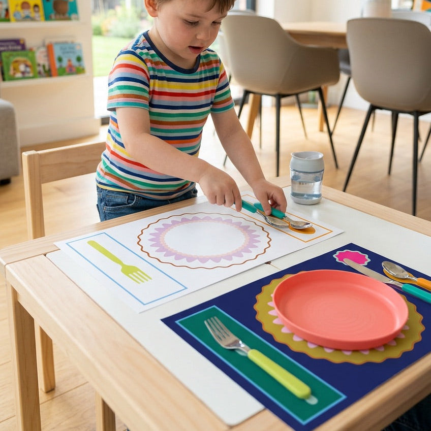 Child playing with colorful paper placemats and cutlery at a table in a bright room.