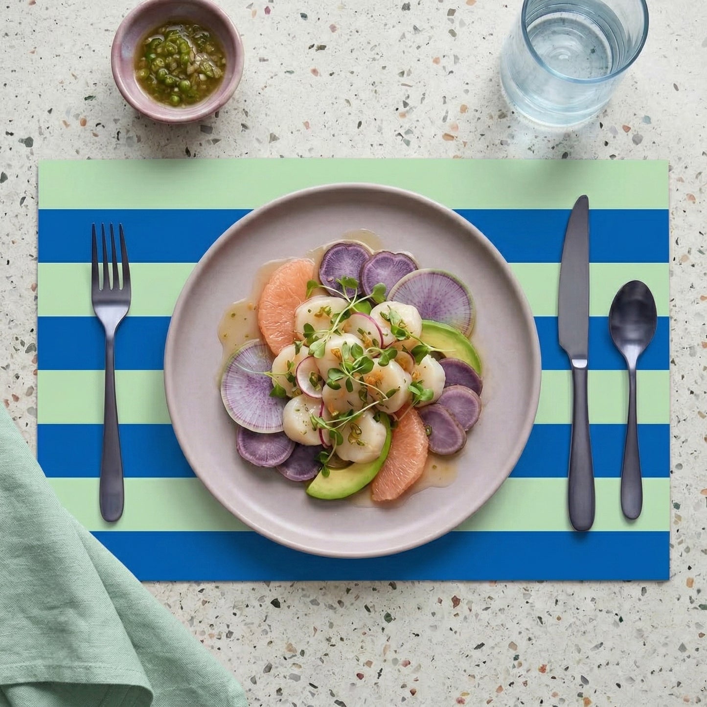 Plated dish with colorful vegetables on a blue and green striped paper placemat with cutlery and a glass of water.