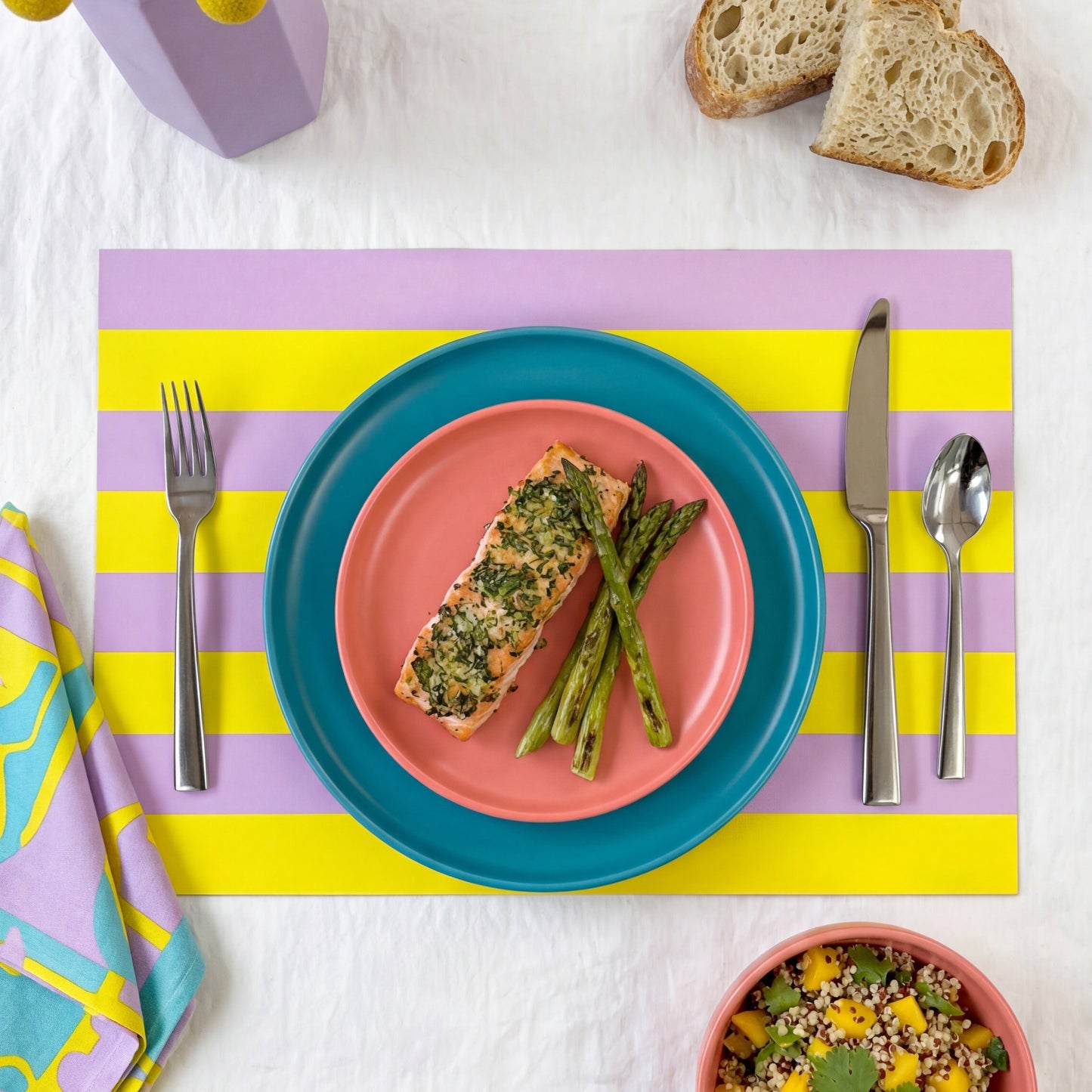 Colorful table setting with plates, bowls, and utensils on yellow and lavender striped paper placemat.