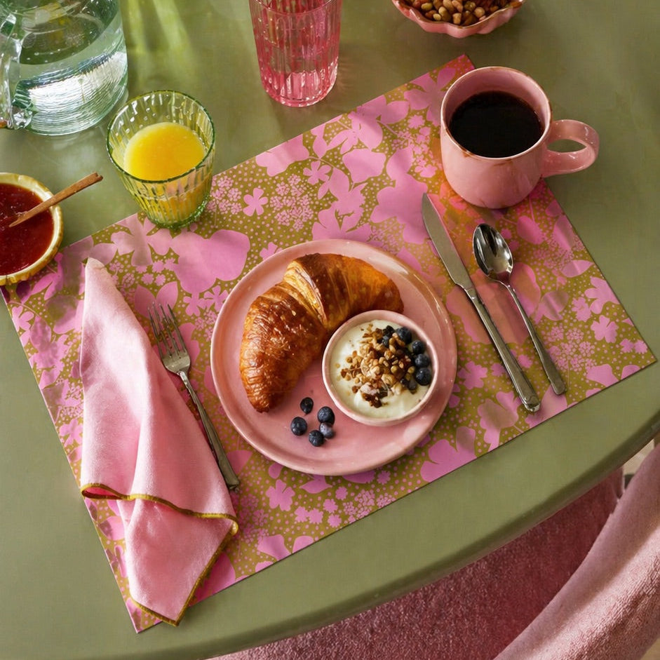 Floral-patterned paper placemat with cutlery on a green table.