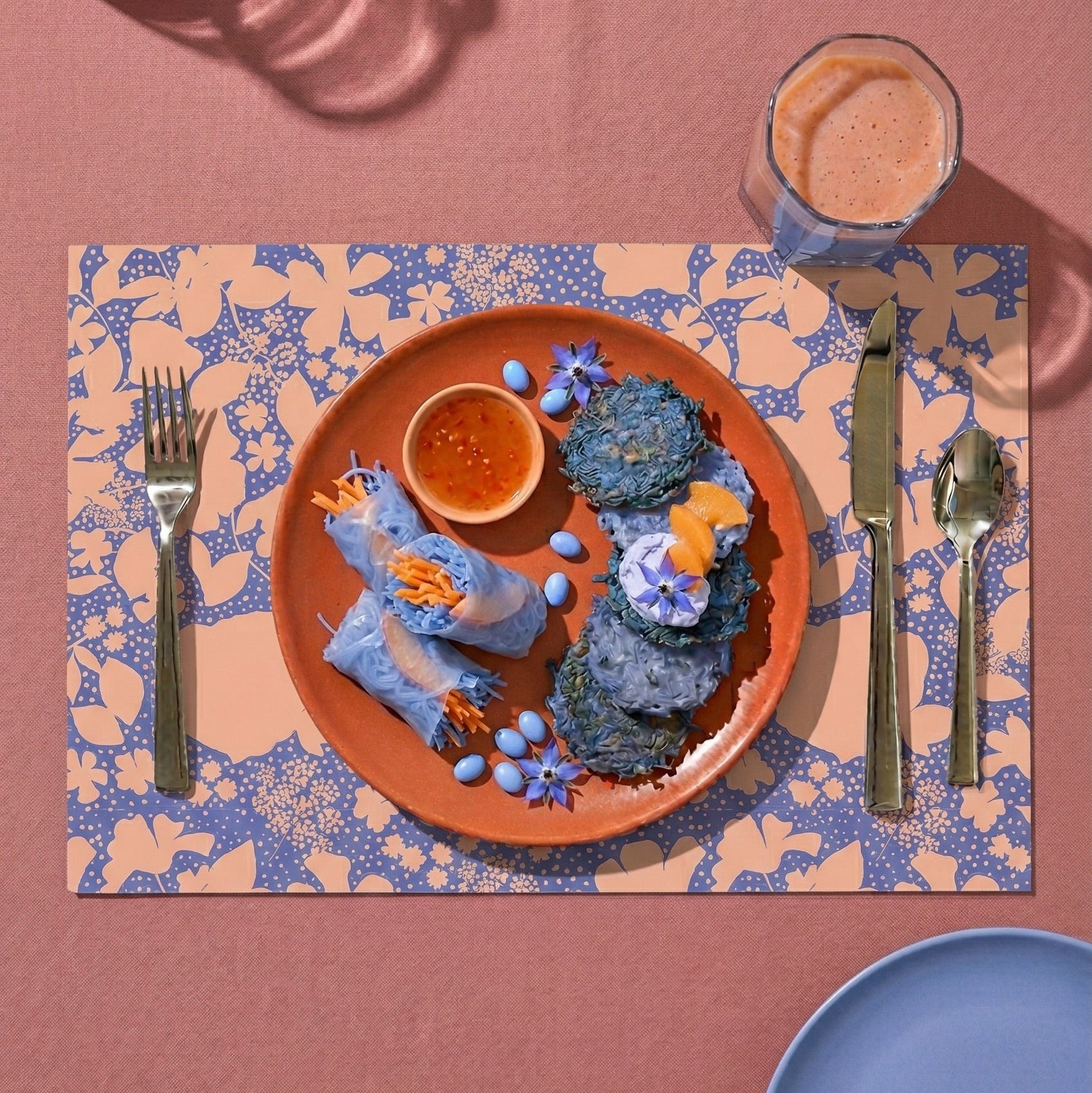 Floral-patterned paper placemat with cutlery on a pink tablecloth.