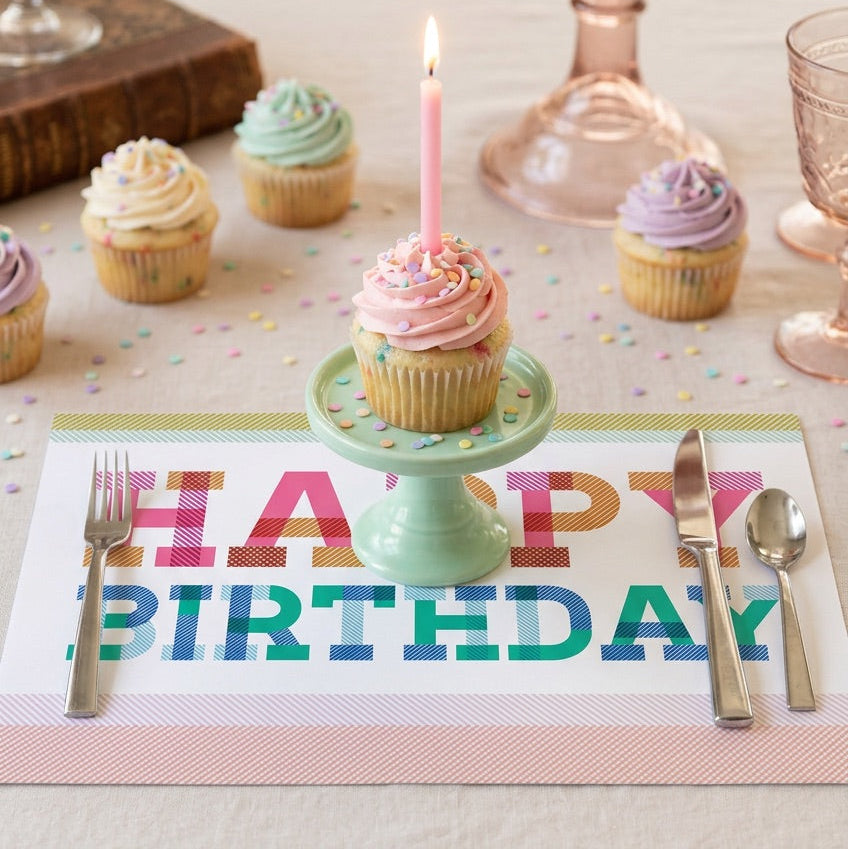 Happy birthday paper placemat on a table with a birthday cake. 