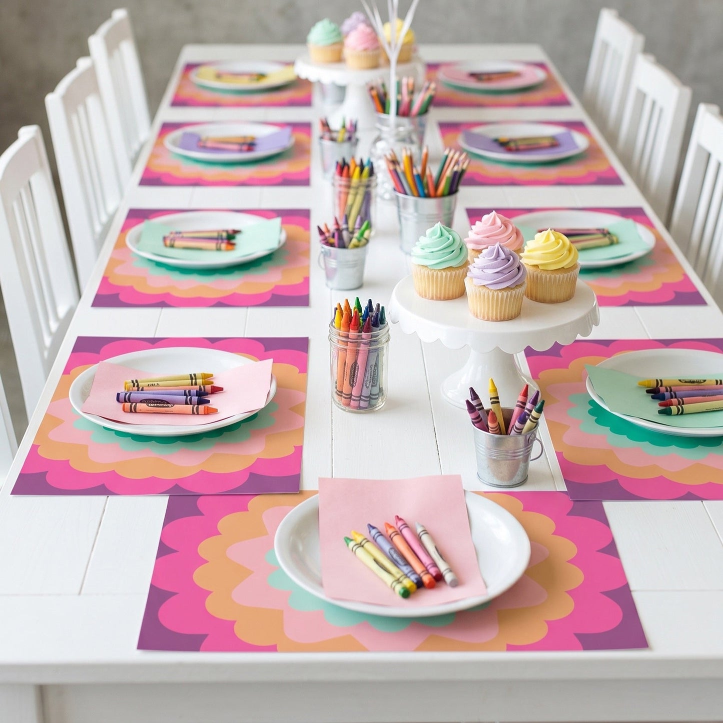 Children's birthday party setup with colorful balloons, cupcakes, crayons, and place settings paper placemats.