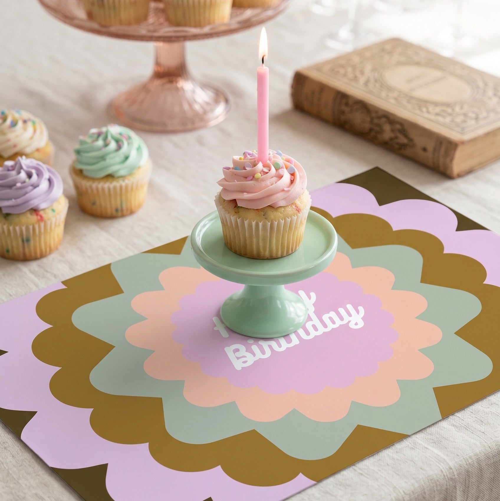 Decorative birthday placemat with a cupcake and candle on a table.