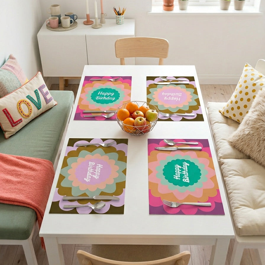 Dining table with colorful paper placemats and a bowl of fruit in a bright room.