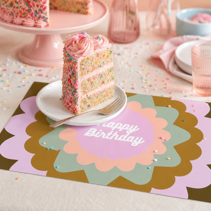 Birthday cake with a slice on a decorative paper placemat with 'Happy Birthday' text, surrounded by party decorations.