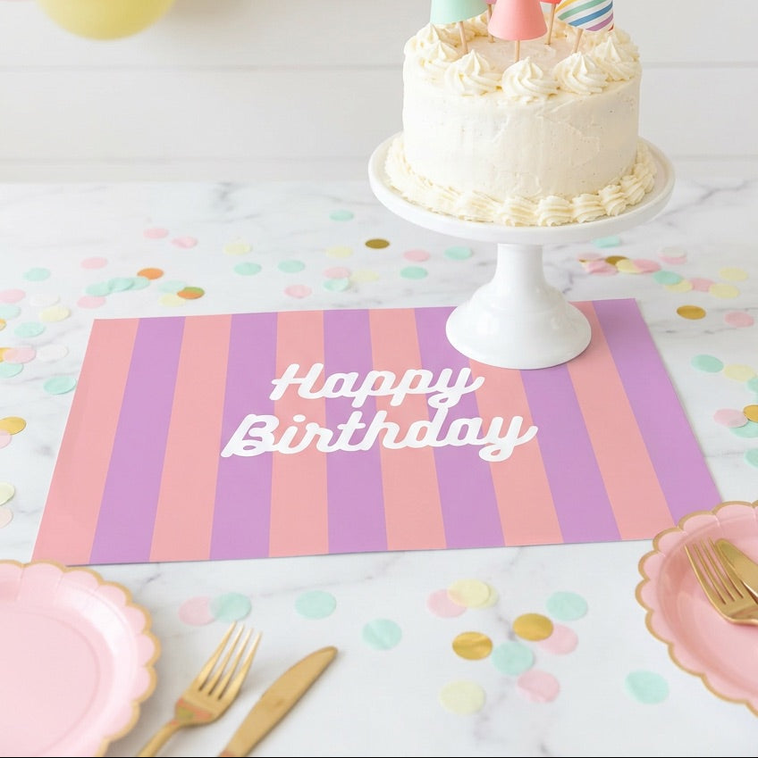 Birthday cake on a white stand, surrounded by balloons and a 'Happy Birthday' placemat.