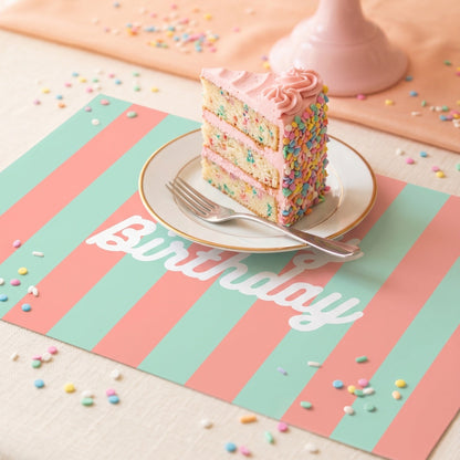 Colorful birthday cake with a slice on a plate, placed on a 'Happy Birthday' paper placemat.