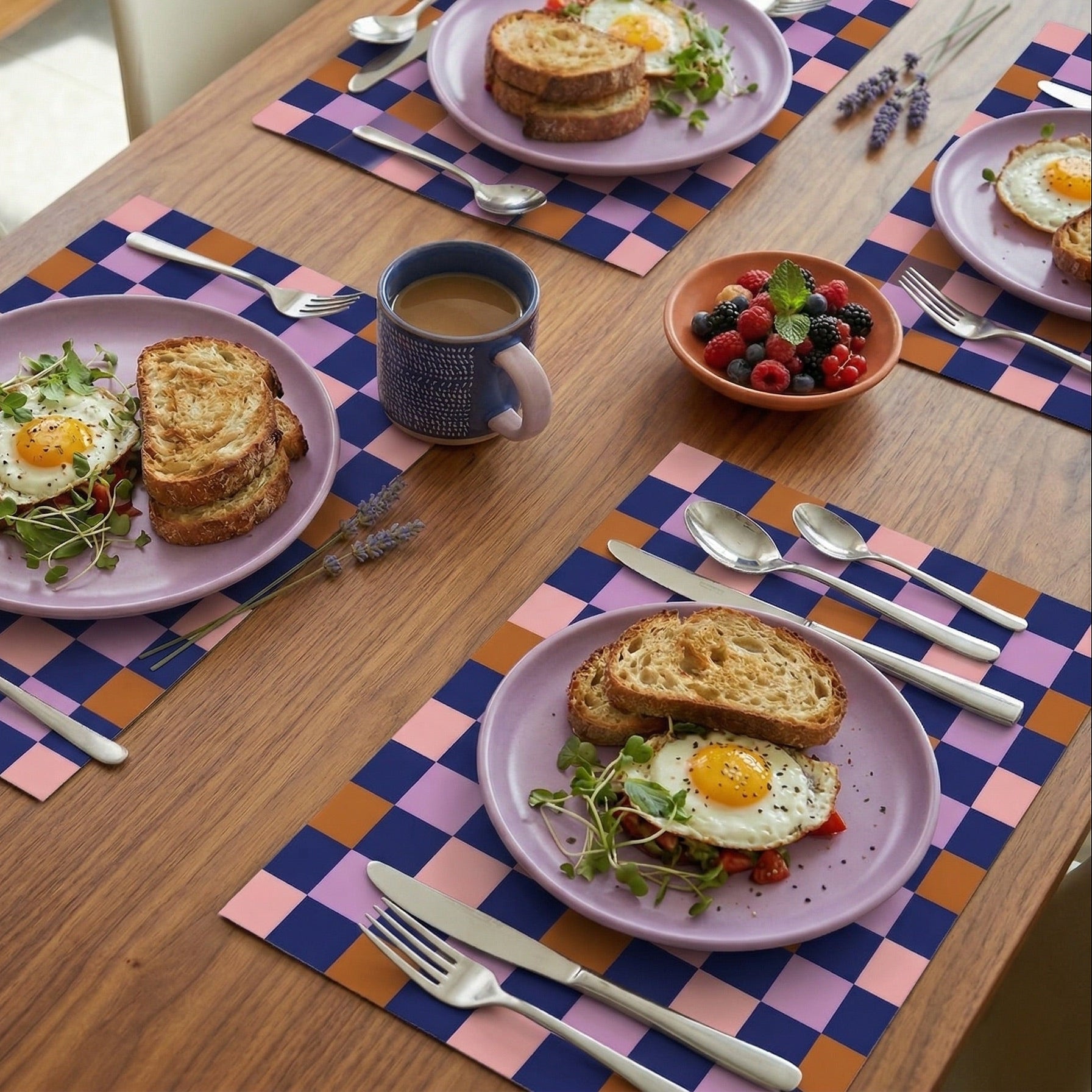 Table setting with plates of food, coffee, and berries on checkered paper placemats.