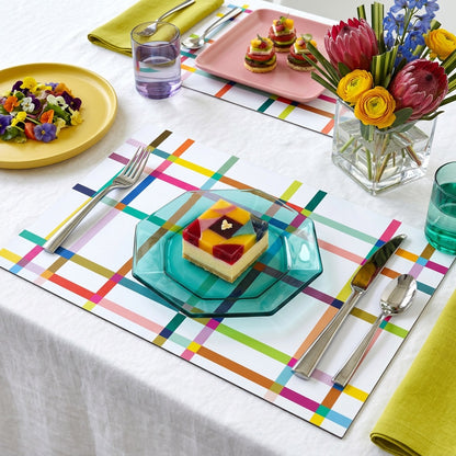 Colorful table setting with a cake on a glass plate, flowers in a vase, and colorful paper placemats.