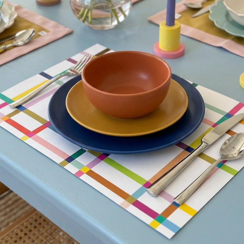 Colorful table setting with plates, bowls, and cutlery on a colorful paper placemat.
