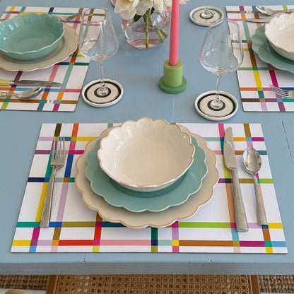 Colorful table setting with plates, glasses, and flowers on colorful paper placemats.