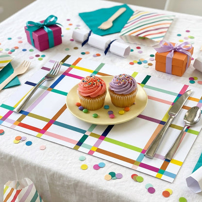 Colorful table setting with cupcakes on a plate, gift boxes, and decorative paper placemats.